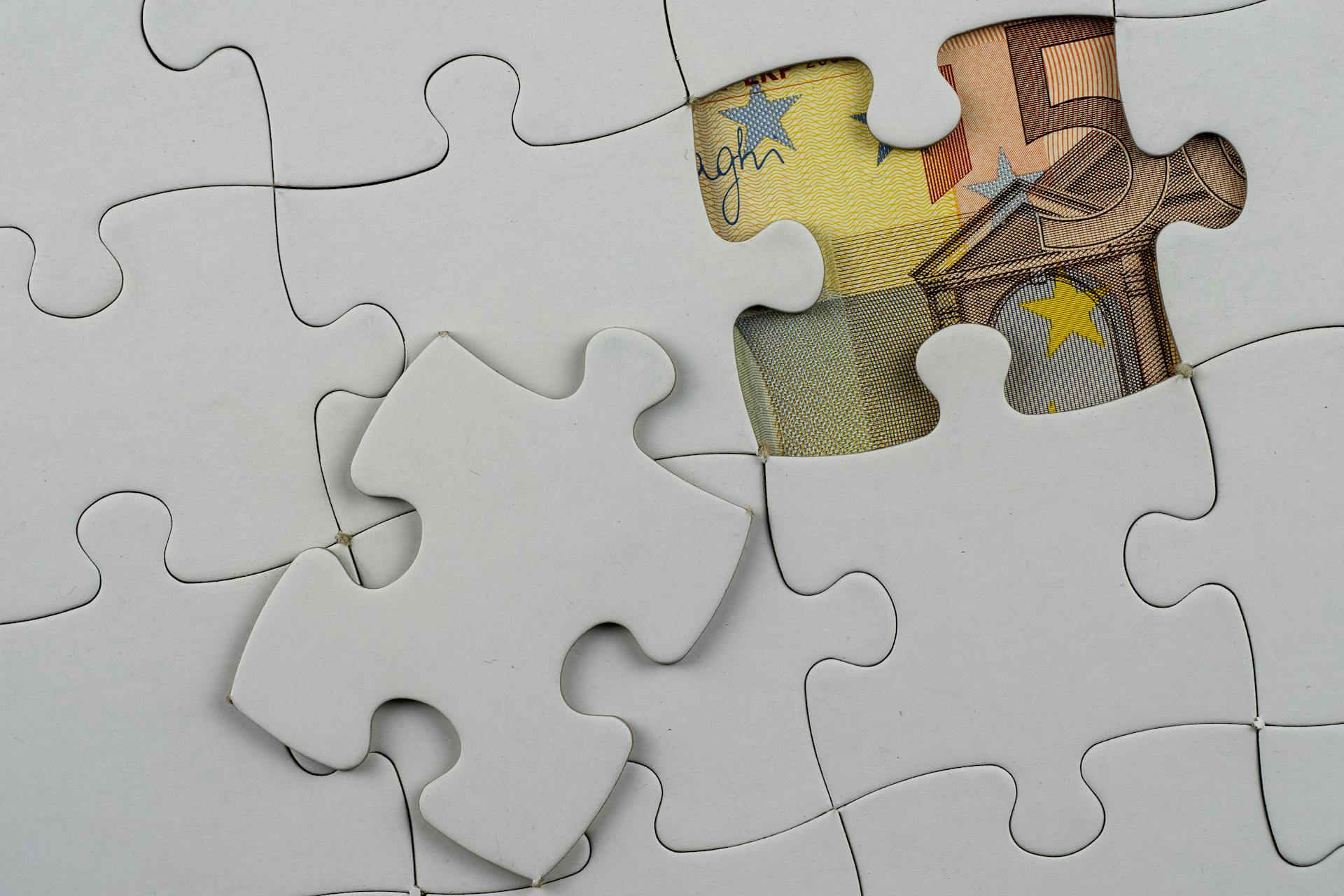 Close-up of a jigsaw puzzle missing piece revealing Euro currency underneath.