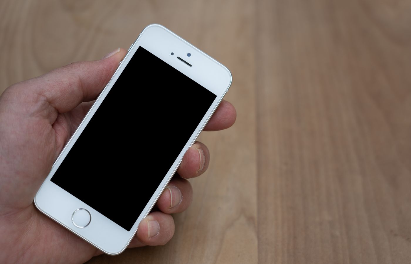 A person holding a smartphone with a blank screen over a wooden surface. Great for mockup use.