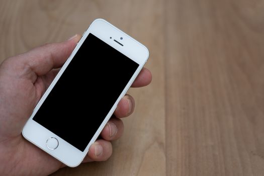 A person holding a smartphone with a blank screen over a wooden surface. Great for mockup use.