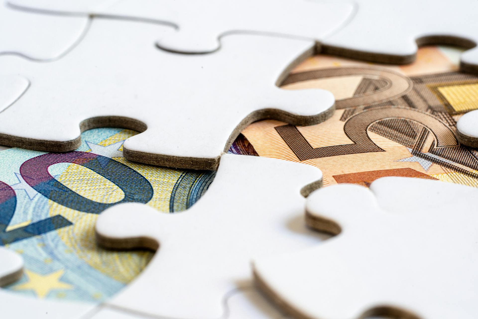 Close-up of euro banknotes revealed under puzzle pieces, symbolizing financial solutions.