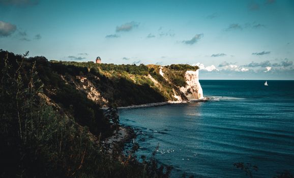 Scenic view of Putgarten chalk cliffs with lighthouse and sailboat on a clear day.
