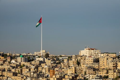 Free View of Amman's cityscape featuring the towering Jordanian flag under a clear sky. Stock Photo