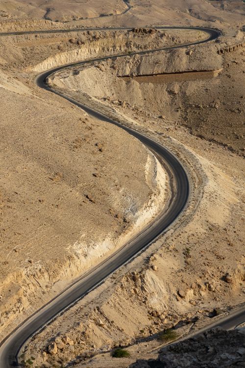Free A curvy road meanders through a dry, rugged desert terrain, captured from above. Stock Photo