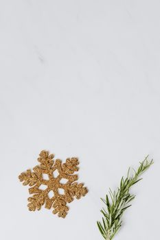 A gold glitter snowflake with a sprig of rosemary on a minimalist white background.
