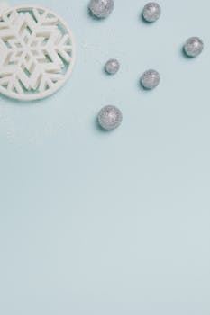 将圣诞装饰品、雪花装饰和银色小玩意平放在淡蓝色表面上