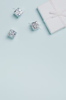 简约的白色和银色礼物平面优雅地铺设在柔软的蓝色背景上，留有充足的复制空间