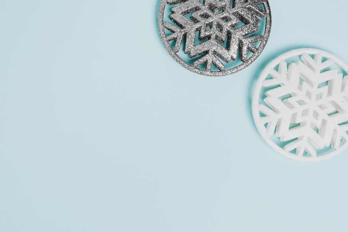 two minimalist snowflake decorations on a pastel blue background