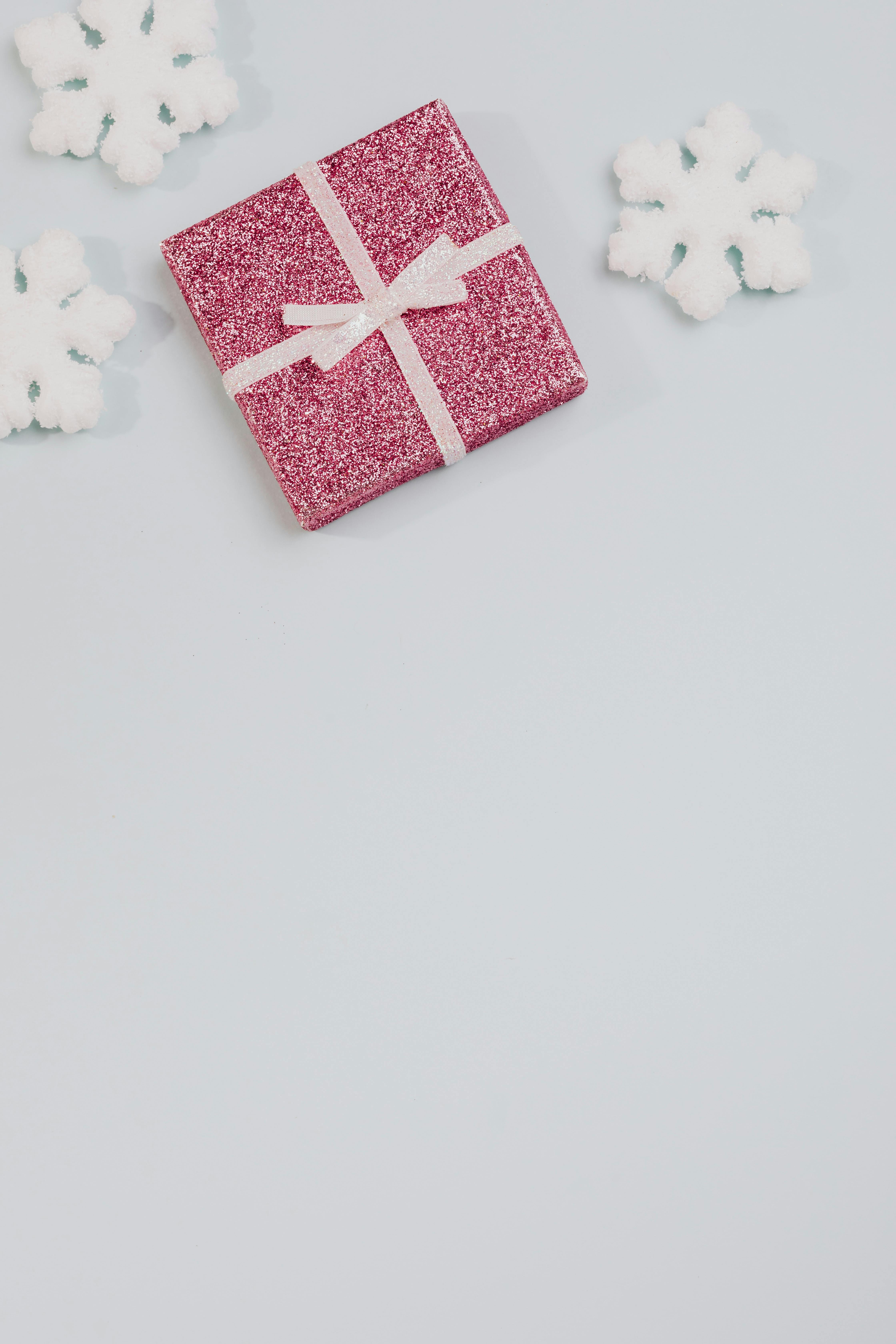 浅色背景上，雪花飘落，一个闪闪发光的粉红色礼品盒，非常适合节日主题