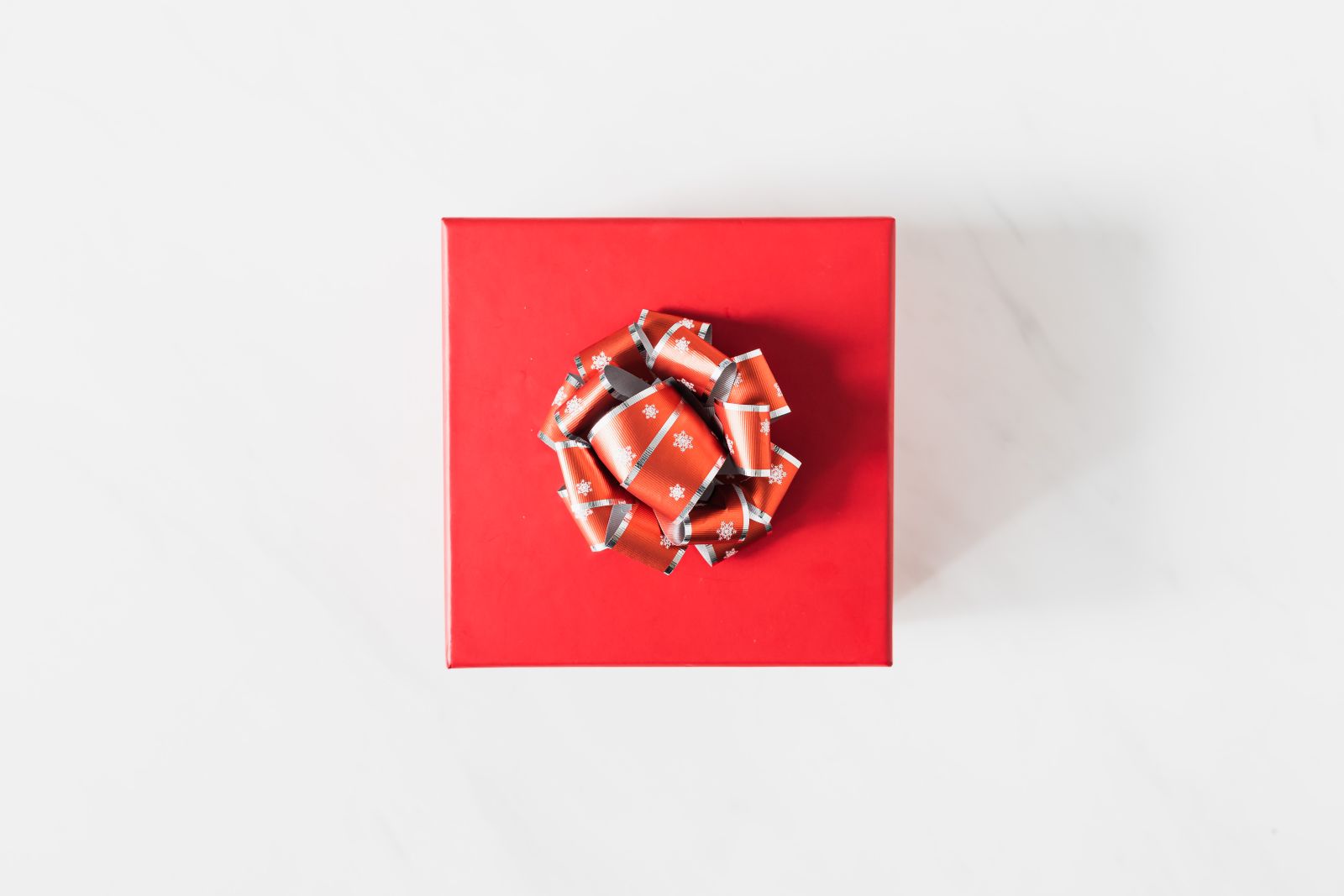 A top view of a vibrant red gift box adorned with a decorative bow on a white background.