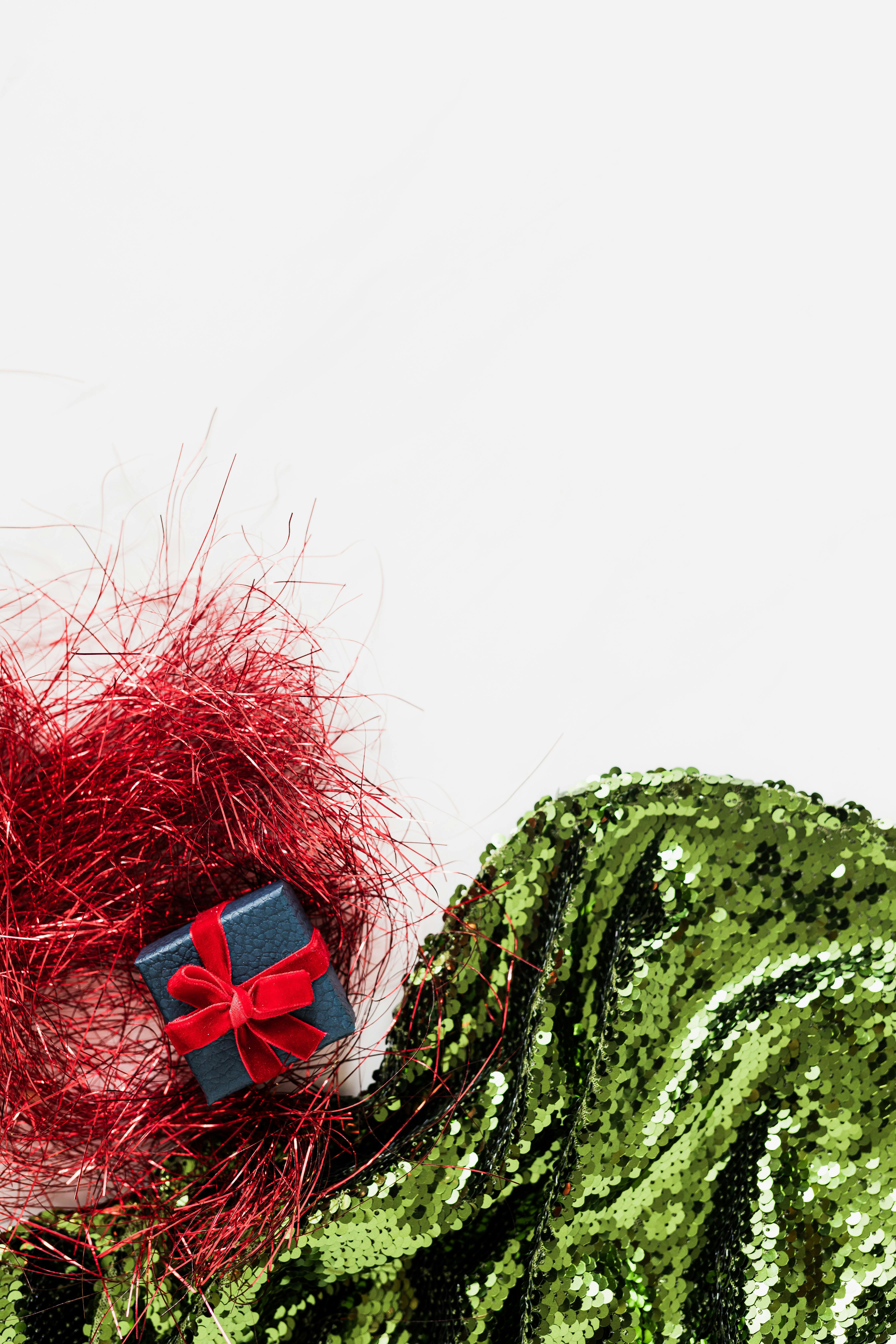 礼物的顶部用红色丝带包裹，并饰有绿色亮片面料，非常适合节日主题