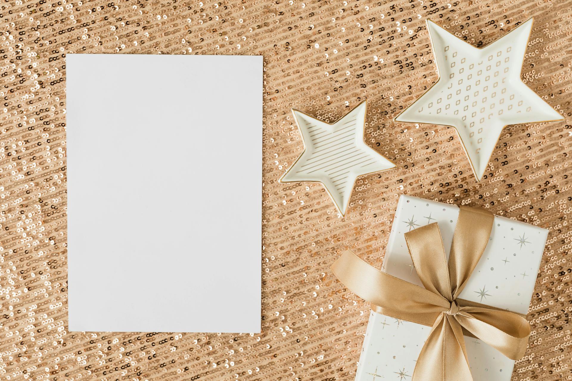 A stylish flat lay of a wrapped gift and star-shaped decor on shimmering gold sequins, perfect for holiday themes.