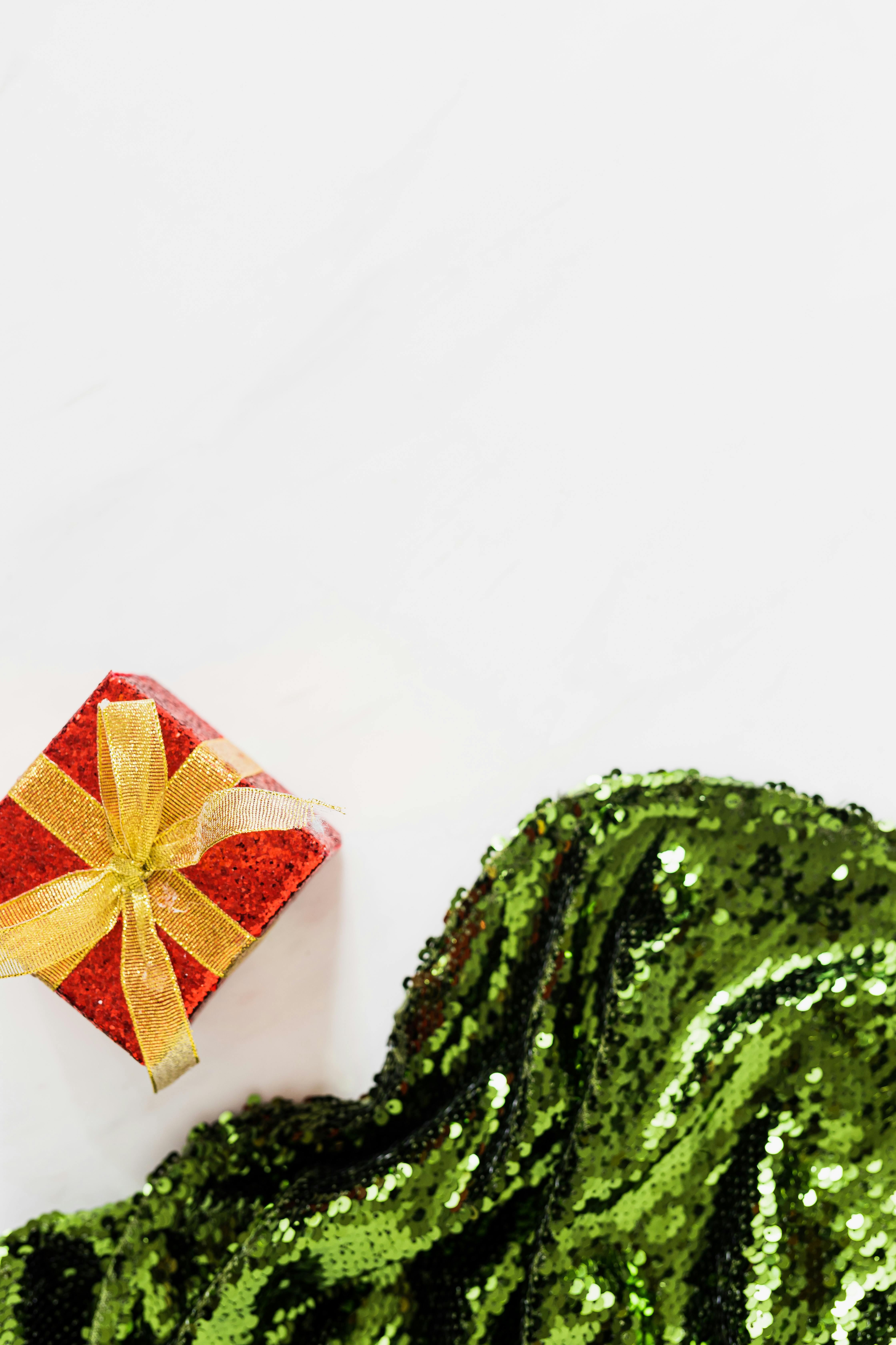 红色礼品盒配上白色背景上的金丝带和绿色亮片织物，非常适合节日主题