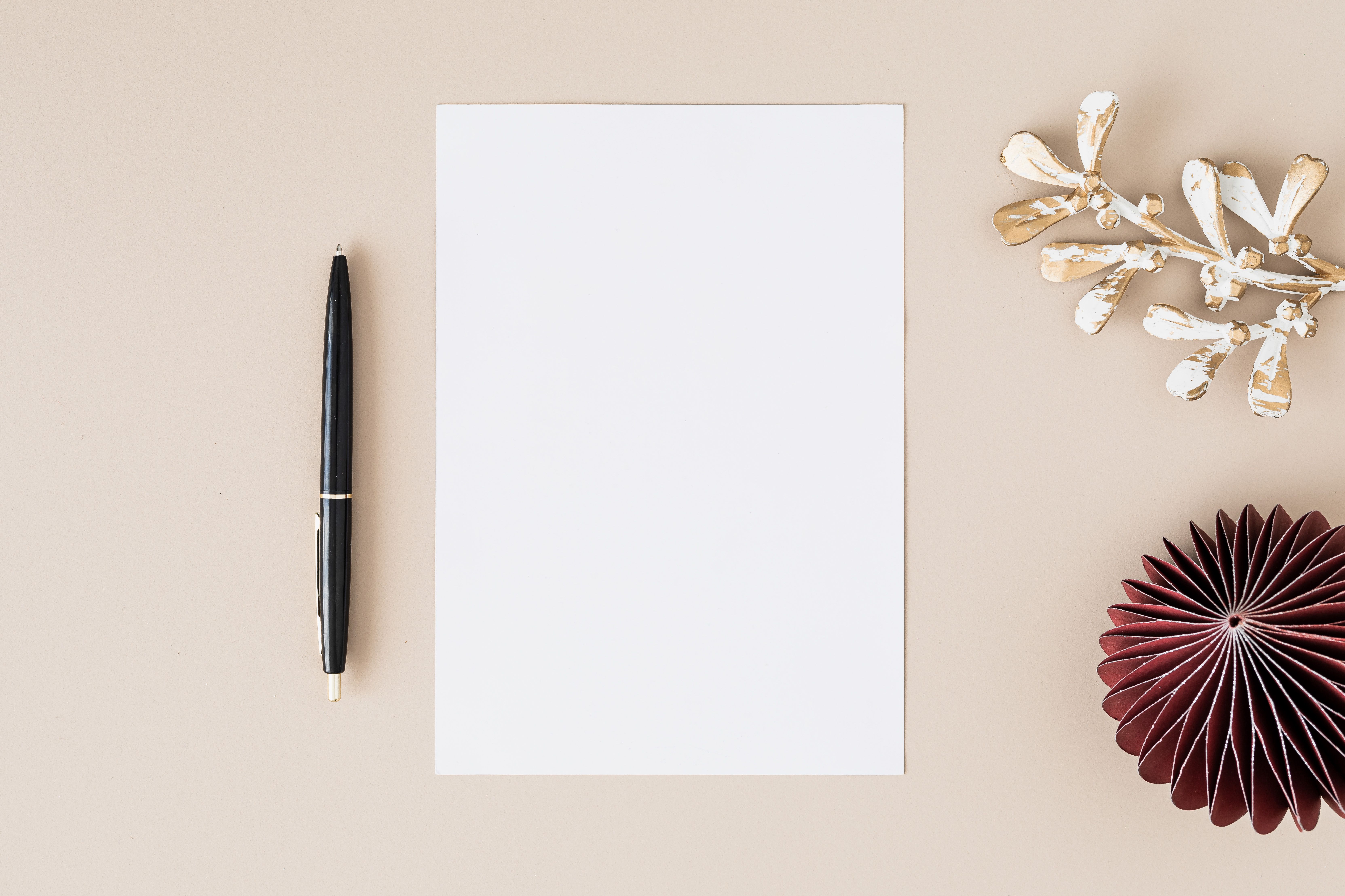 Elegant flatlay with blank paper, black pen, and decorative elements on beige — letterheads