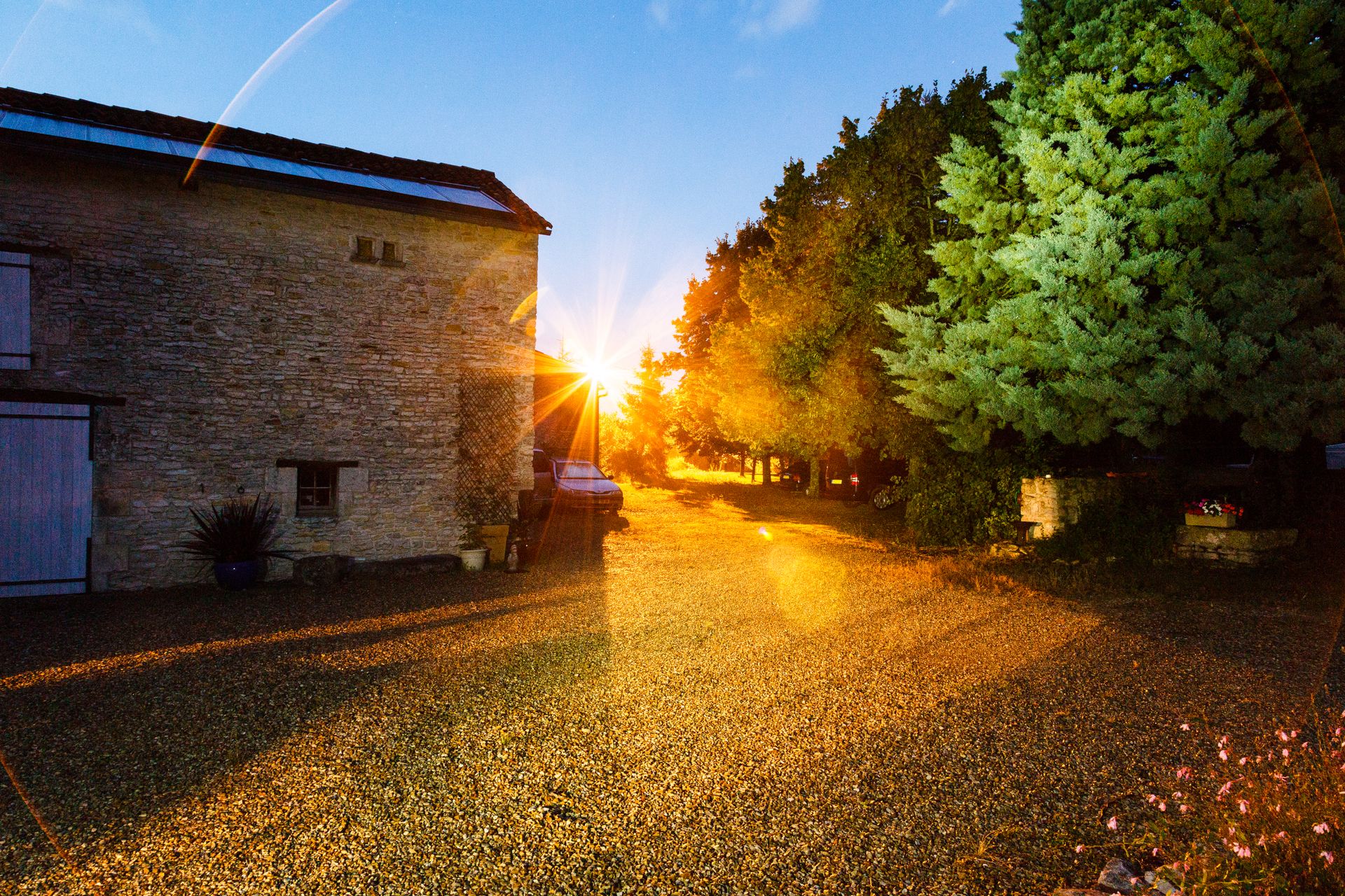 Scenic sunset illuminating a rustic farmhouse in Nouvelle-Aquitaine, France, with vibrant trees and gravel road.