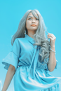 From below tender Asian female in silk blue dress with long dyed hair looking away on blue background