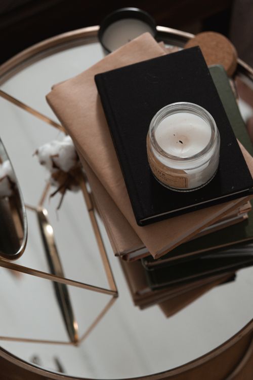 Free A cozy setup featuring a stack of notebooks and a candle on a mirrored table. Stock Photo