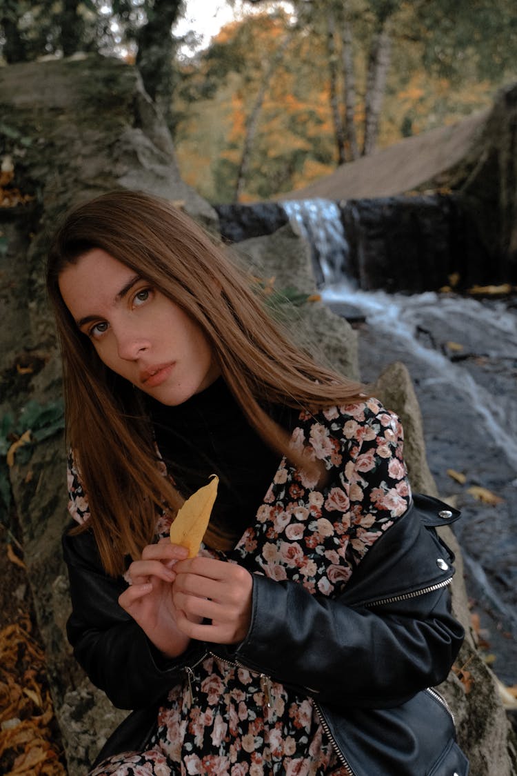 Stylish Focused Woman With Autumn Leaf Near Waterfall In Forest