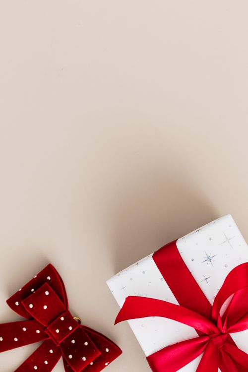 Free A minimalist image featuring a gift box with a red ribbon and bow on a beige background, perfect for festive celebrations. Stock Photo