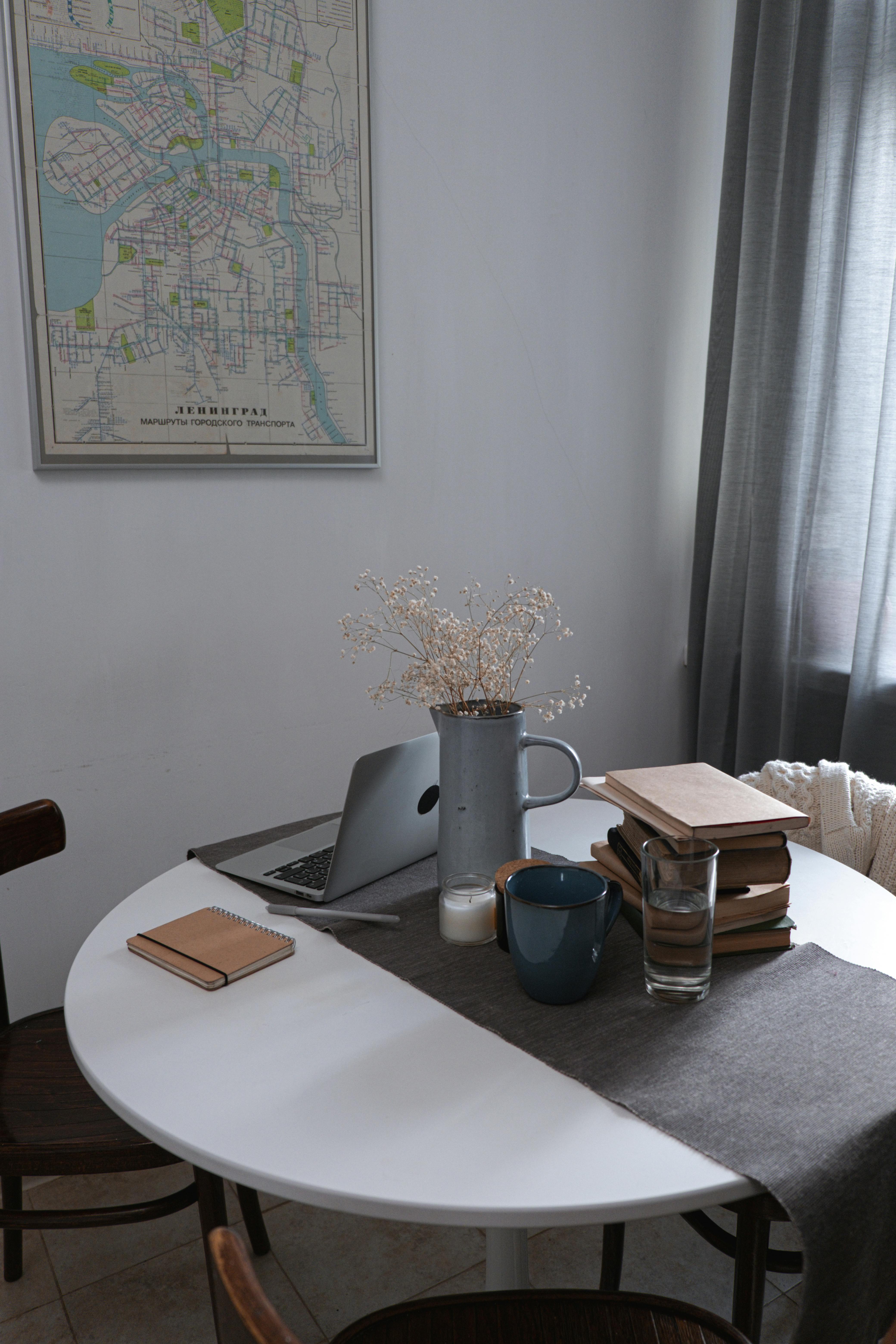 家庭办公室布置得很舒适，圆桌上摆着一堆书籍、笔记本电脑和一个陶瓷花瓶