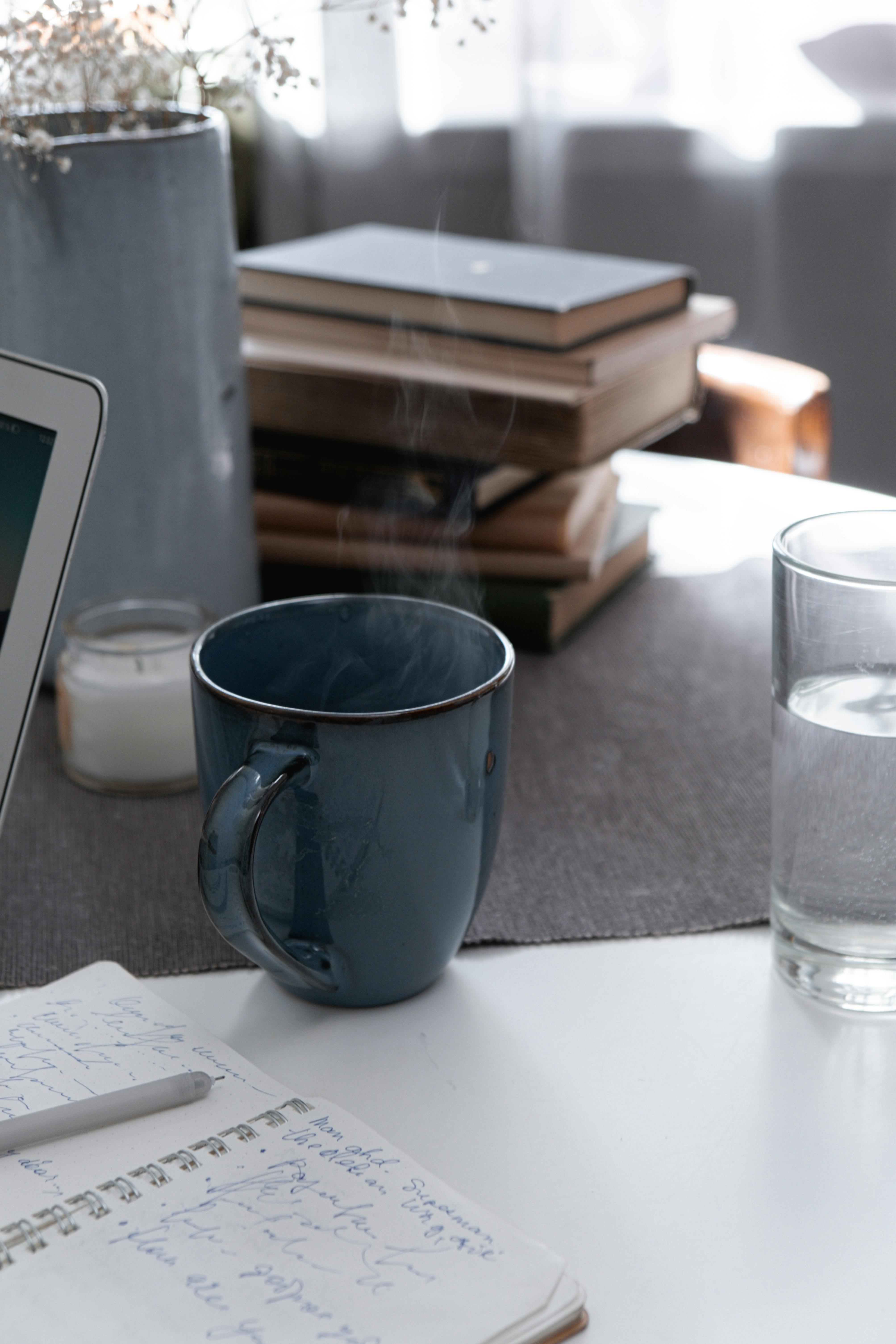 室内工作空间宁静，配有热气腾腾的咖啡杯、笔记和堆叠的书籍