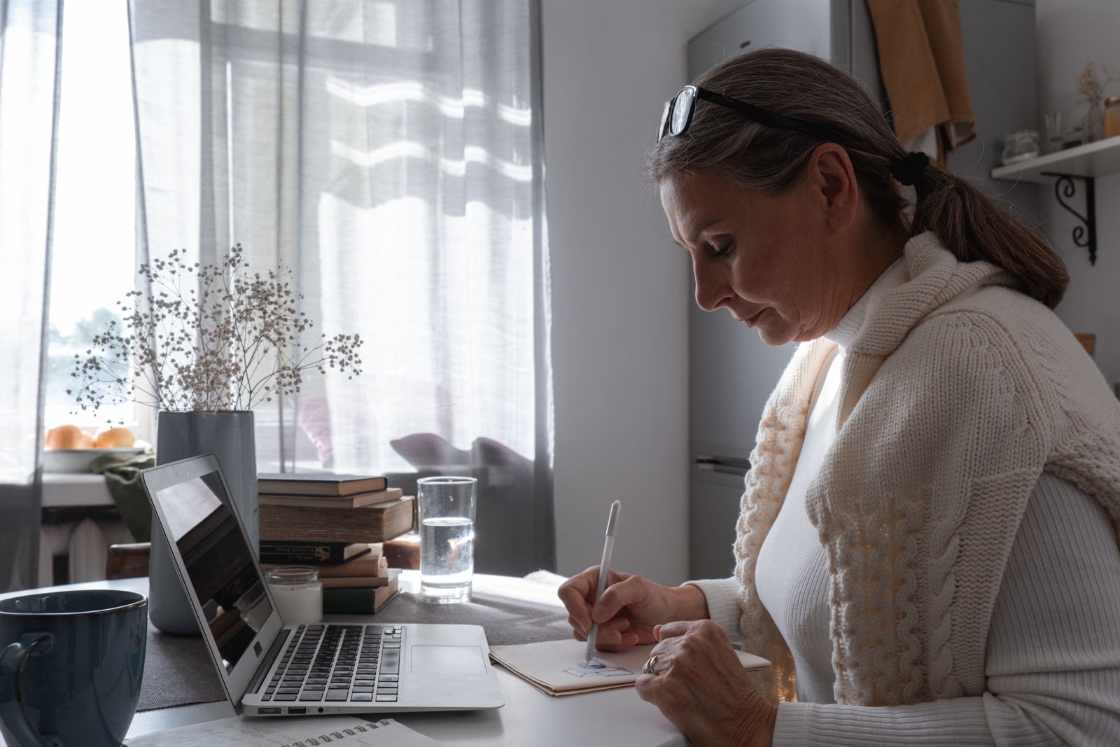 Someone in a knitted jumper writing notes at a desk beside a laptop — photo by cottonbro studio on Pexels