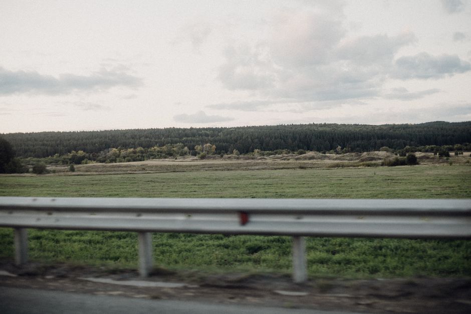 Expansive countryside landscape with road barrier and dense forest in the background under cloudy sky.