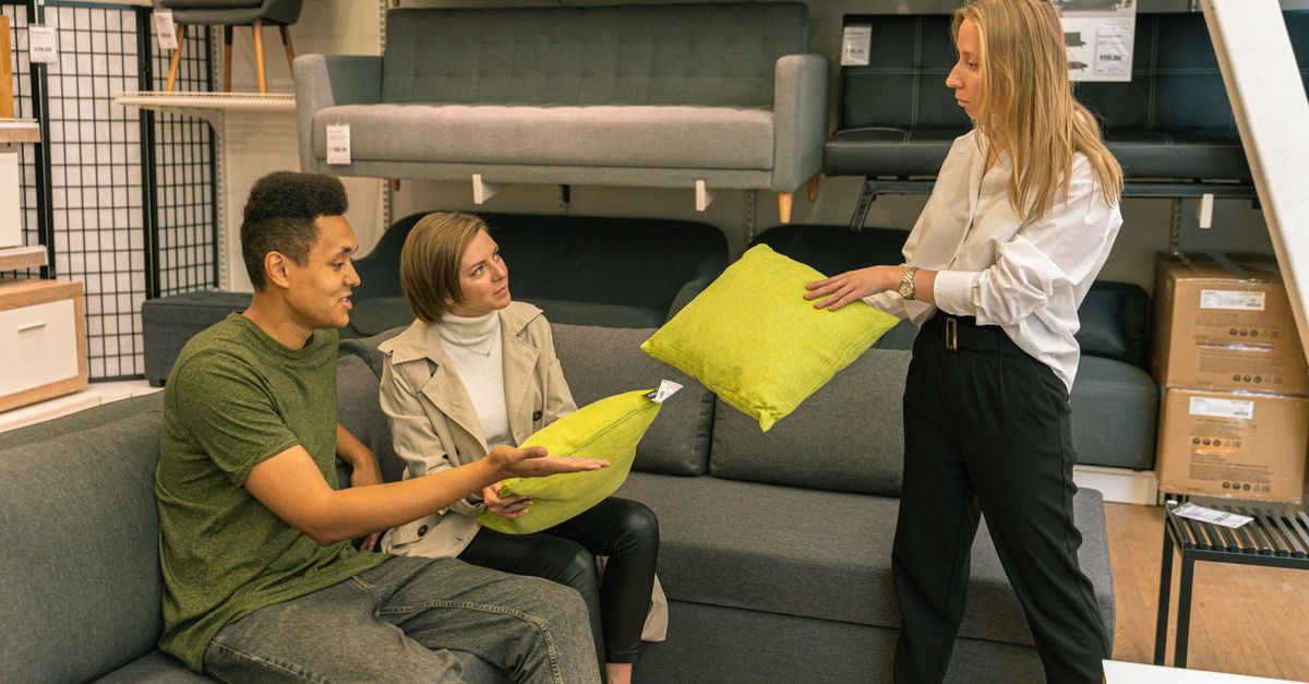 A couple selecting cushions with a salesperson in a furniture store, surrounded by sofas.