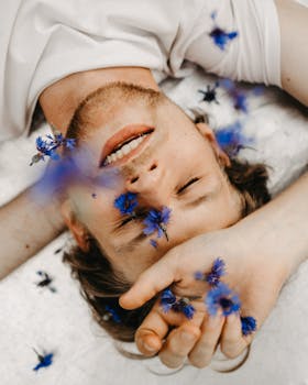 一名男子闭着眼睛，摆出宁静的姿势，躺在蓝色矢车菊中