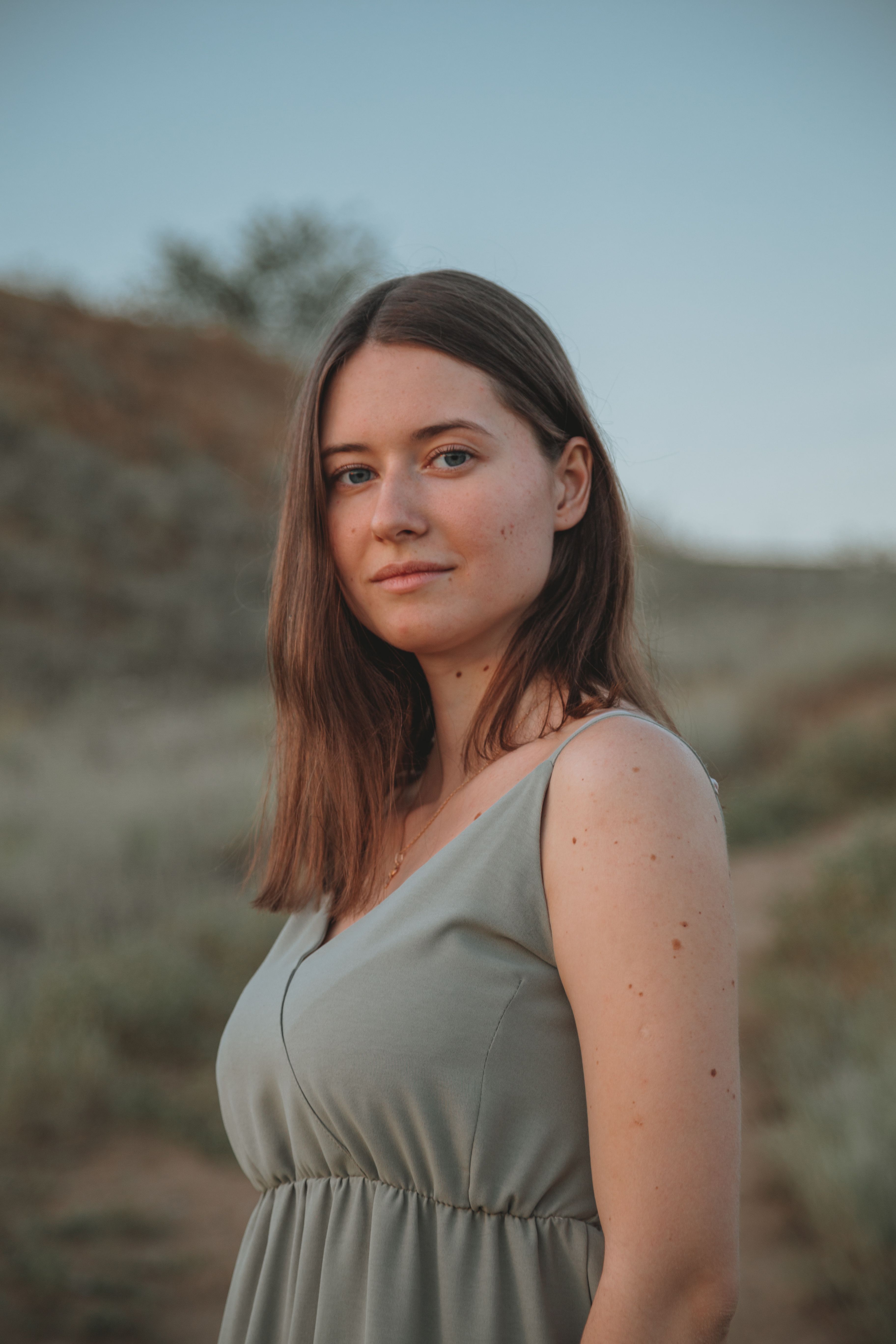 Cheerful female wearing casual clothes looking at camera while standing in nature near hilly terrain against blue sky on blurred background
