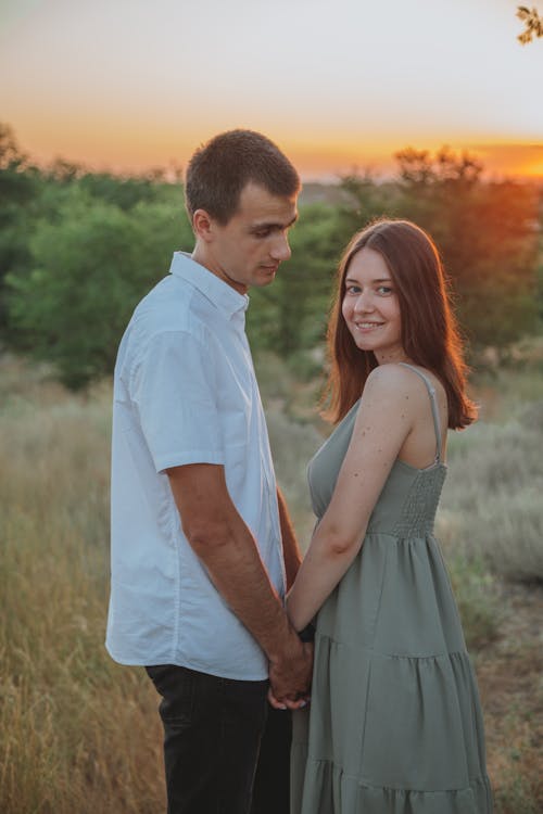 Pasangan Muda Yang Bahagia Bergandengan Tangan Di Padang Rumput Saat Matahari Terbenam