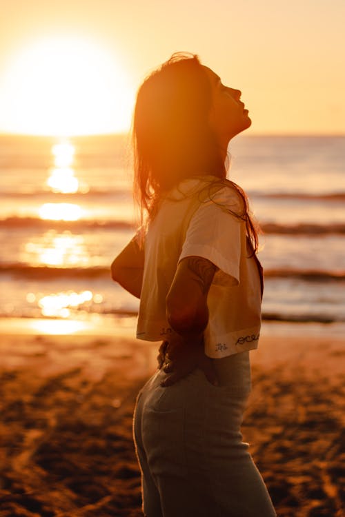 Free Woman in White Shirt Standing on Beach during Sunset Stock Photo
