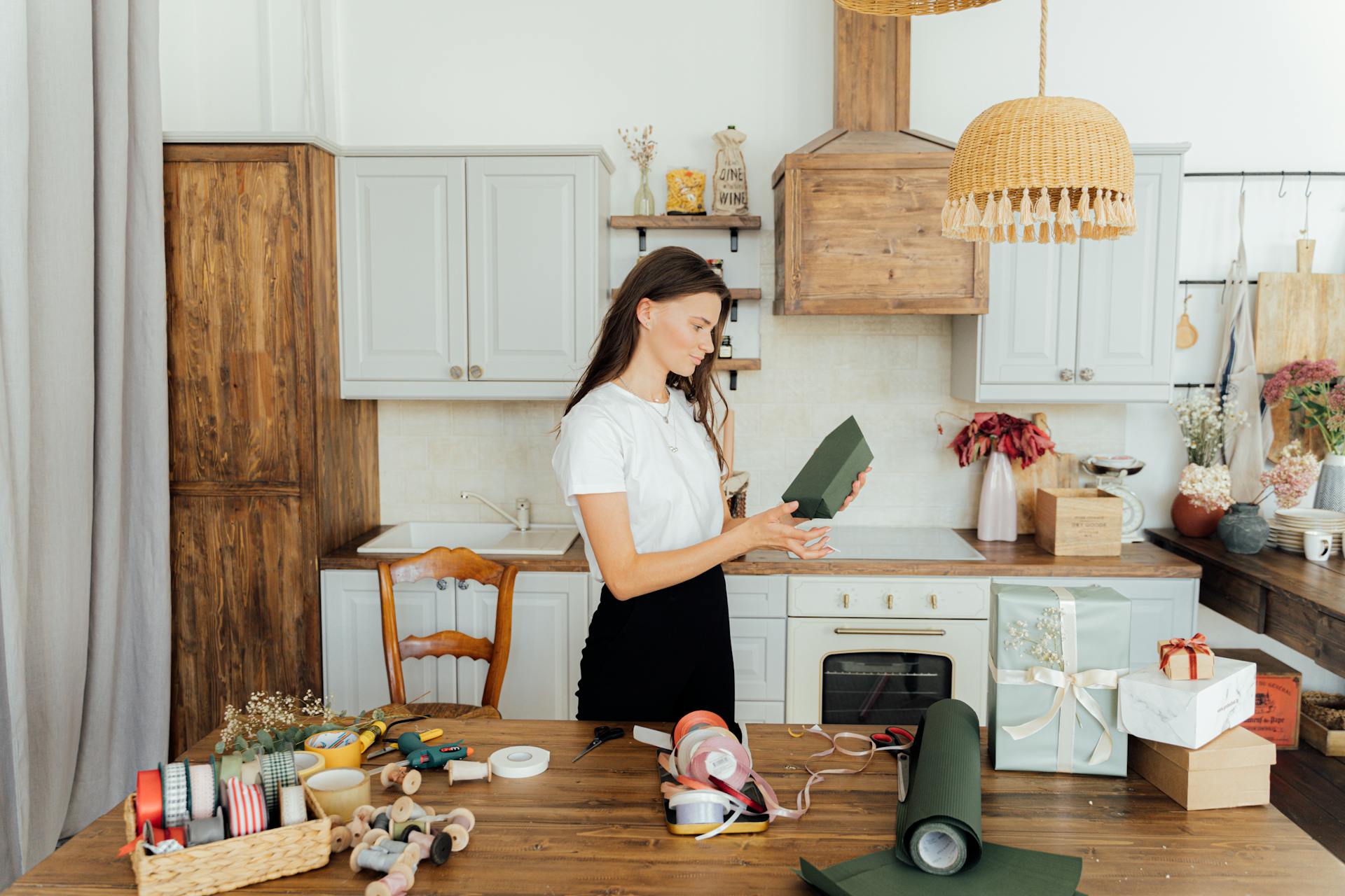 A woman wrapping presents in a cozy kitchen with ribbon and paper around.