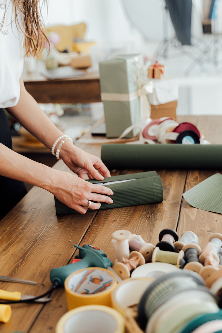 A Person Wrapping A Gift On A Wooden Table