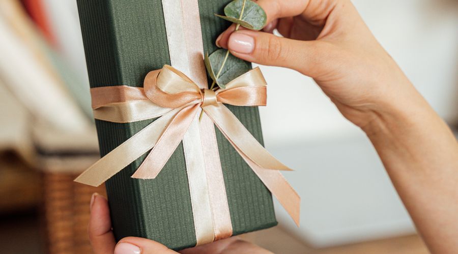 Personne tenant un cadeau emballé avec un ruban, prêt à offrir un bijou