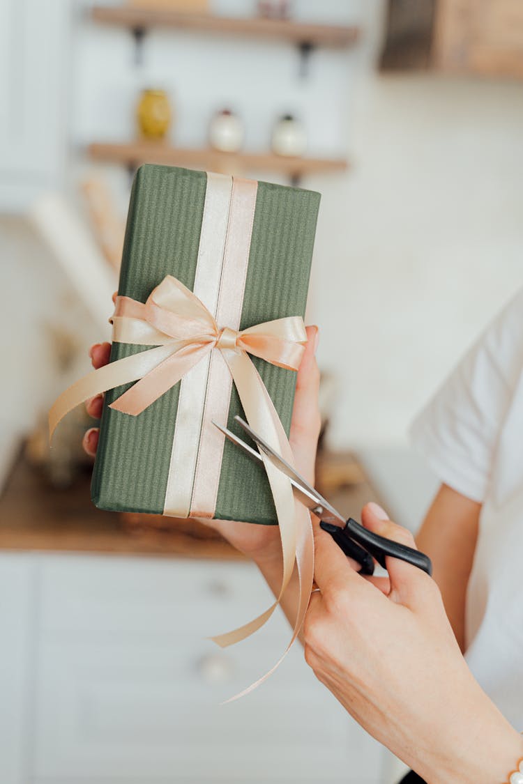 A Person Cutting A Ribbon On The Gift 