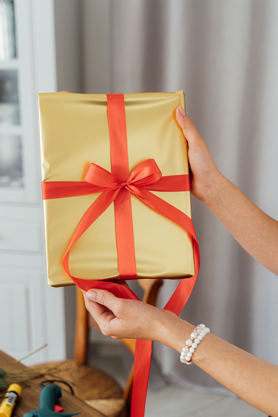 Hands holding a gold-wrapped gift box tied with a red ribbon bow
