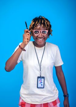 Cheerful woman in casual attire holding a pen with eyeglasses and ID badge against a vibrant blue background.