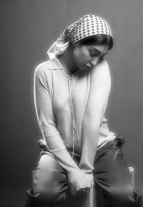 A Grayscale Photo of a Woman in White Long Sleeves Sitting while Looking Down