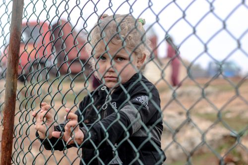 Free Sad ethnic child standing near metal net against freight car and looking at camera Stock Photo