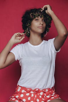Stylish woman with curly hair and hoop earrings posing confidently against a vibrant red background.
