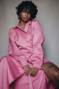 Portrait of a woman in a pink dress posing against a gray background.
