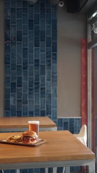 A delicious burger with fries and a beer placed on a wooden table in a modern restaurant setting.