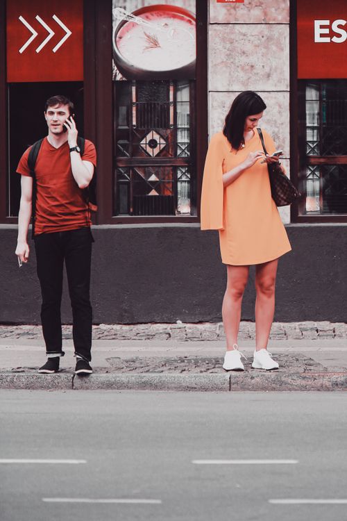 Free A man and woman stand on a city sidewalk using their phones. Stock Photo