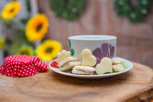 Heart-shaped biscuits accompany a ceramic cup of tea on a wooden table with a floral backdrop.