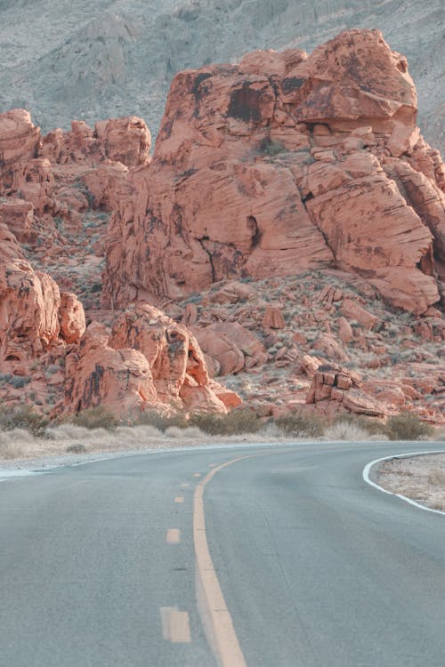 Narrow asphalt roadway leading to red rocky formations in canyon in daylight in nature in mountainous area in summer day