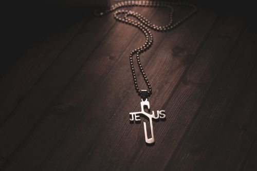 Free Close-up of a silver Jesus cross necklace on a dark wooden background, evoking spirituality and faith. Stock Photo