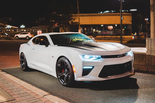 Modern white sports automobile with luminous headlights on asphalt roadway in city at dusk