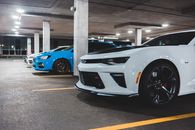 Front bumpers of contemporary luxury autos under roof with shiny lamps on asphalt parking in evening
