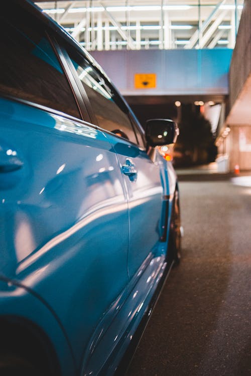 Contemporary shiny blue car with tinted glass on asphalt roadway near urban building in evening