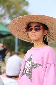 一个自信的年轻女孩戴着大遮阳帽和红色太阳镜，在户外享受阳光明媚的一天